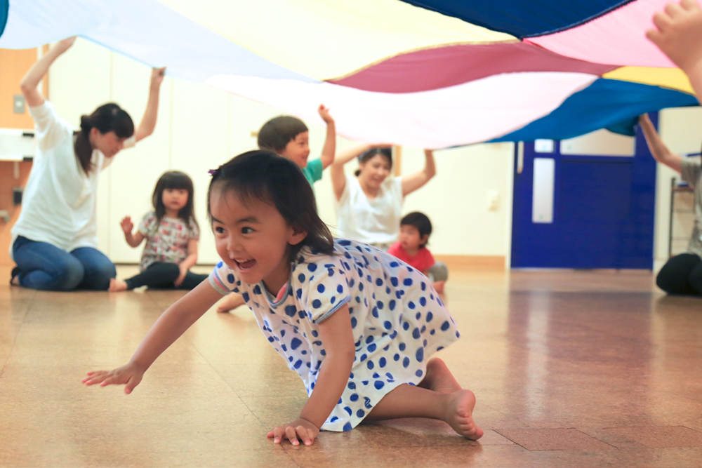 大きなカラフルな布の下を楽しそうにくぐる子供の様子