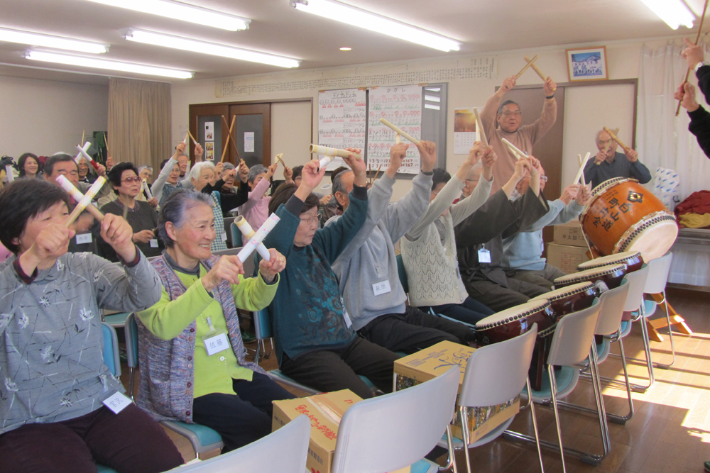 健康づくり講座に参加する地域のみなさん。太鼓を叩く体操の様子。